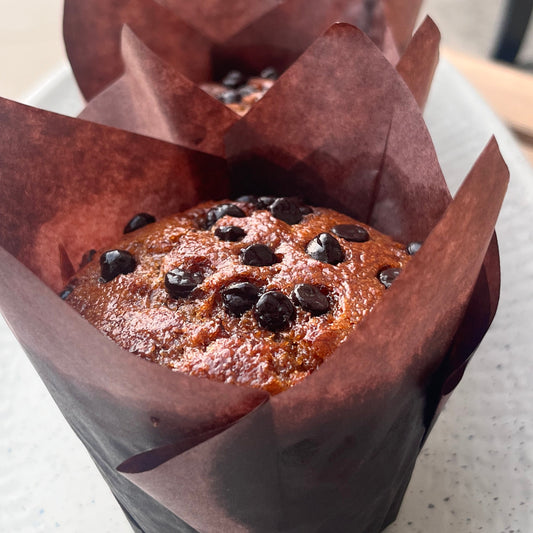 Chocolate muffin with chocolate chips in a brown paper wrapper on a white surface
